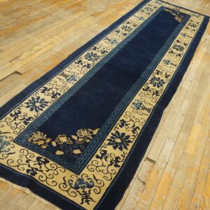 Dark blue runner rug with wide beige borders, blue and gold floral patterns, rests on distressed wood planks.