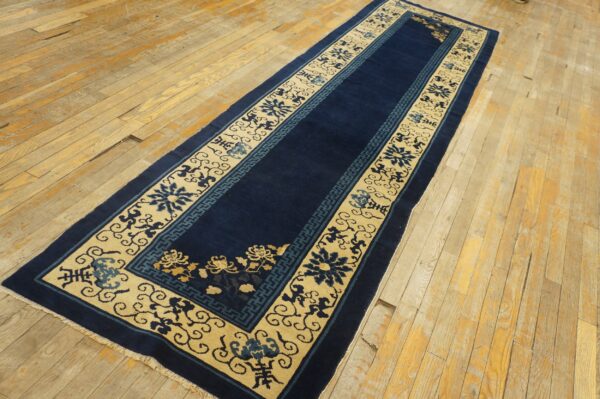 Dark blue runner rug with wide beige borders, blue and gold floral patterns, rests on distressed wood planks.