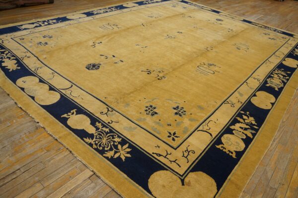 A large gold rug with a wide navy blue patterned border lies on distressed wooden floorboards.