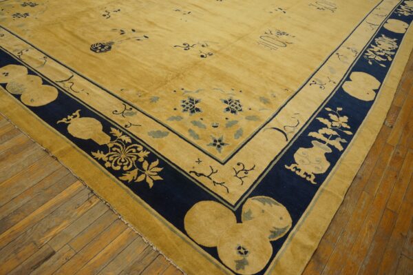 Corner of a golden-yellow rug with navy blue and light blue patterns resting on rustic wood floors.
