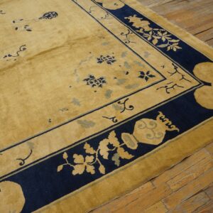 A gold rug with stylized navy and light blue designs rests on worn hardwood floors.