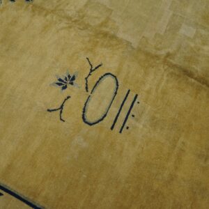 Close-up of a mustard yellow rug featuring stylized navy blue abstract floral motifs.