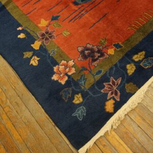 Close-up of a rust-colored rug with a dark blue floral border resting on distressed hardwood floors.