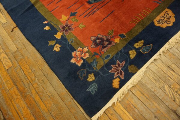 Close-up of a rust-colored rug with a dark blue floral border resting on distressed hardwood floors.