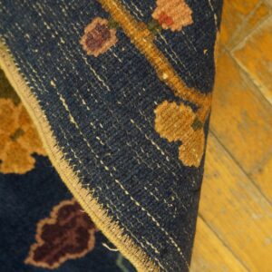 Navy rug with yellow, pink, and burgundy floral motifs, showing the finished edge against golden wood flooring.