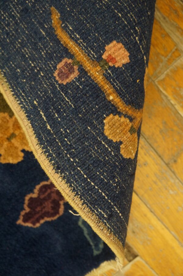 Navy rug with yellow, pink, and burgundy floral motifs, showing the finished edge against golden wood flooring.