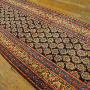 Navy, red, and gold patterned runner rug displayed on a rustic light brown hardwood floor.