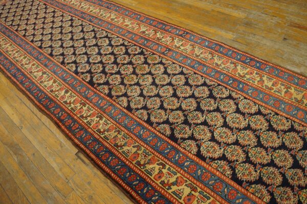 Navy, red, and gold patterned runner rug displayed on a rustic light brown hardwood floor.