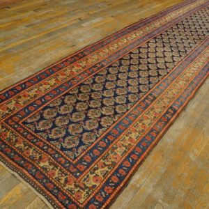 Traditional navy runner rug with rust and gold borders on distressed yellow wood flooring.