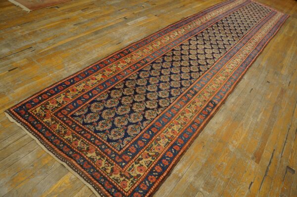 Traditional navy runner rug with rust and gold borders on distressed yellow wood flooring.