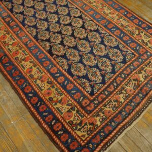 Navy blue rug with dense floral patterns and red-and-yellow borders rests on distressed wood planks.