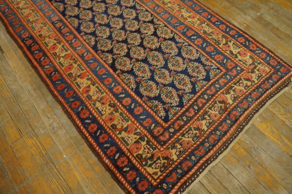 Navy blue rug with dense floral patterns and red-and-yellow borders rests on distressed wood planks.