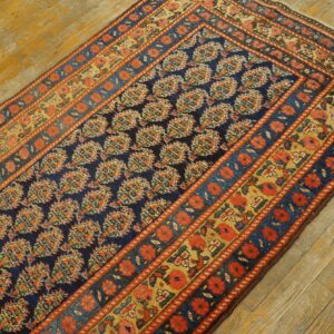 Navy runner with dense floral patterns and orange-red borders rests on rustic, distressed wood flooring.