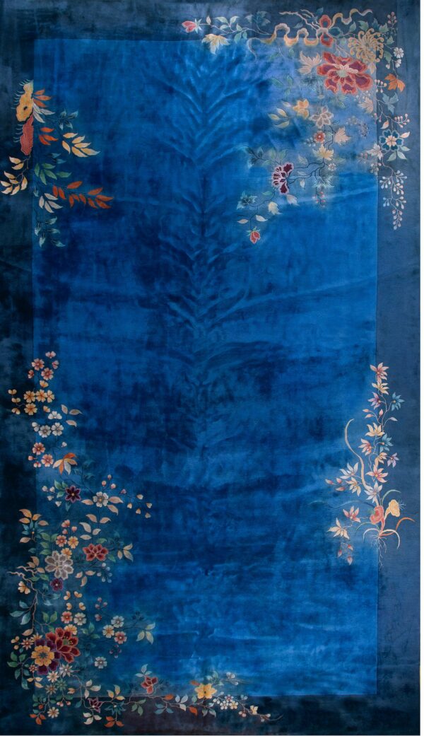 Velvety blue area rug featuring multicolored floral and leaf motifs cascading across the borders.