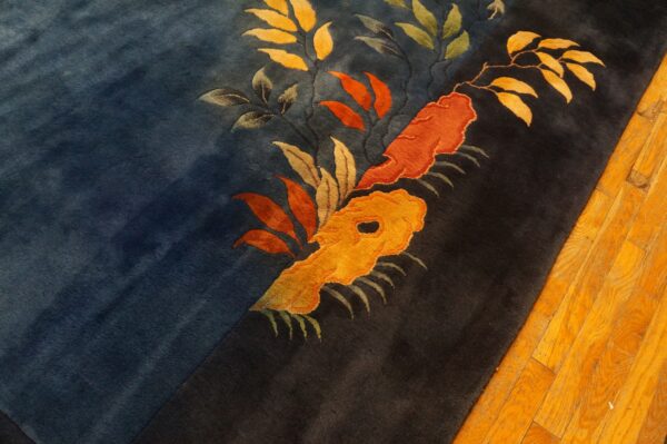 Dark blue and black rug with bold, carved orange and yellow flowers rests on polished wood planks.