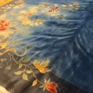 Plush blue rug featuring detailed floral and vine patterns in rust and gold on a wood floor.