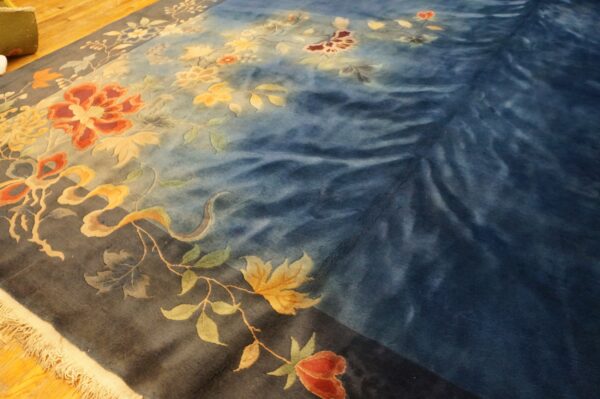 Plush blue rug featuring detailed floral and vine patterns in rust and gold on a wood floor.