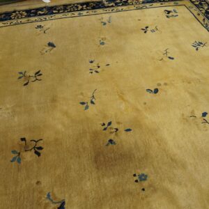 A low-pile gold rug with scattered blue floral motifs and a detailed dark blue border lies on a wood floor.