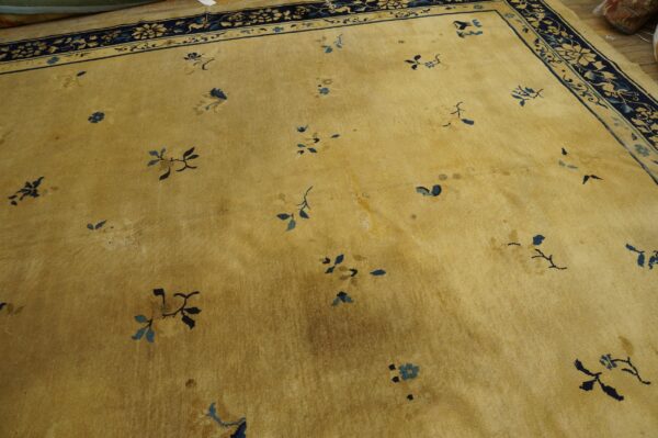 A low-pile gold rug with scattered blue floral motifs and a detailed dark blue border lies on a wood floor.