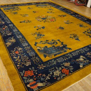 Mustard yellow rug with a navy border displays floral and symbolic patterns on light wood flooring.