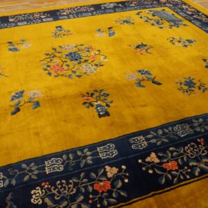 Golden yellow rug with blue, pink, and gray floral sprays and a detailed navy blue border on wood floor.