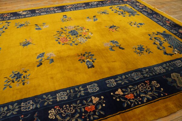 Golden yellow rug with blue, pink, and gray floral sprays and a detailed navy blue border on wood floor.