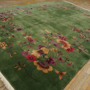 Plush green area rug with pink and gold floral motifs resting on distressed wooden planks.