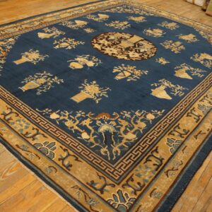 A traditional navy blue rug with gold vase motifs and wide geometric borders sits on light wooden plank flooring.