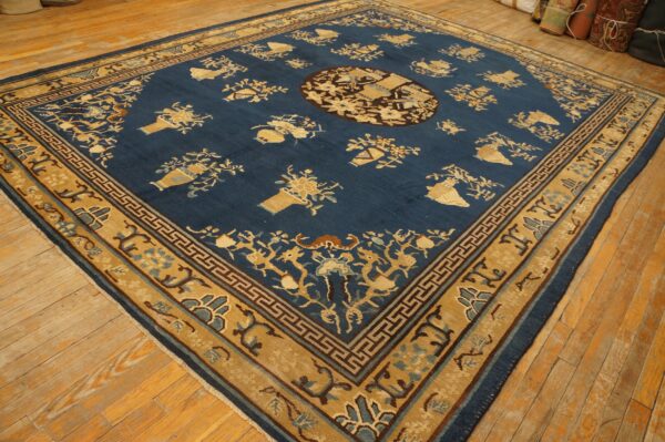A traditional navy blue rug with gold vase motifs and wide geometric borders sits on light wooden plank flooring.