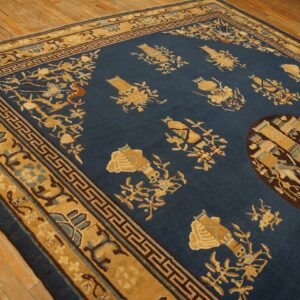 Blue rug with tan floral and vase motifs, dark medallion, and geometric borders on wood floor.