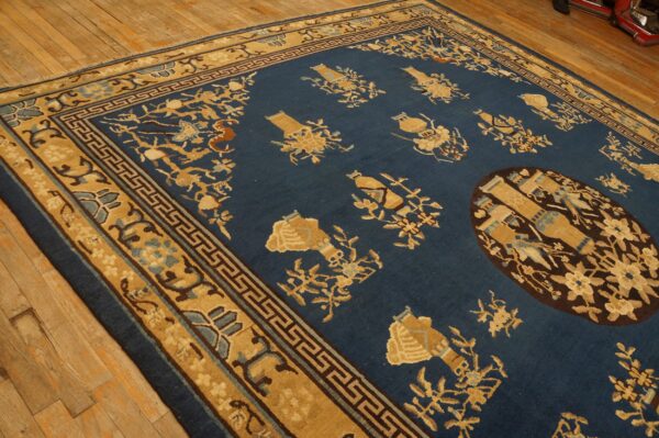 Blue rug with tan floral and vase motifs, dark medallion, and geometric borders on wood floor.