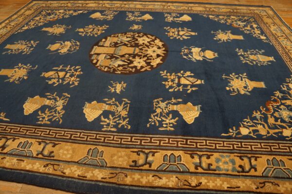 Rectangular deep blue rug with repeating tan vase motifs and a prominent geometric border on wood flooring.