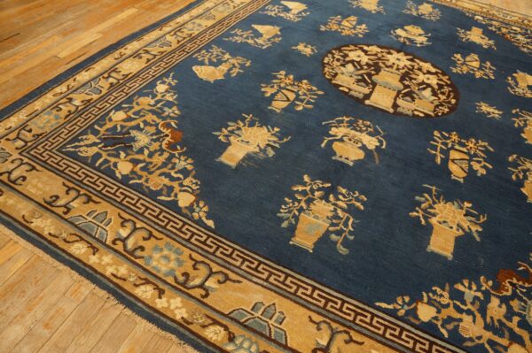 Blue area rug with tan scattered floral urn patterns and a geometric border on light wood floors.