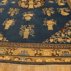 Low-pile blue rug with scattered tan floral arrangements and a wide gold border featuring geometric motifs.