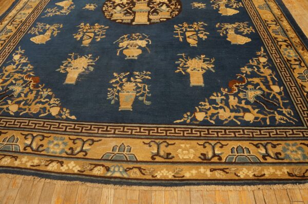 Low-pile blue rug with scattered tan floral arrangements and a wide gold border featuring geometric motifs.