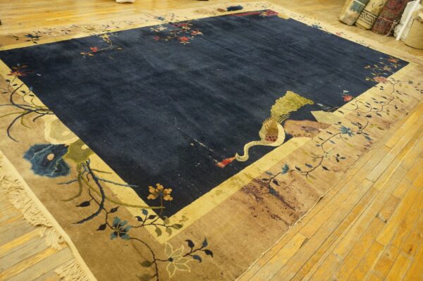 Deep blue rug with an ornate beige border, featuring large flowers and a crane, on hardwood planks.