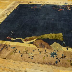 A high-pile navy blue rug featuring a large peacock motif and detailed tan floral borders rests on wood floors.