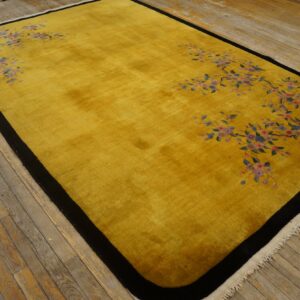 Plush yellow rug with a black frame and pink and blue flowering branches on rustic wooden floors.