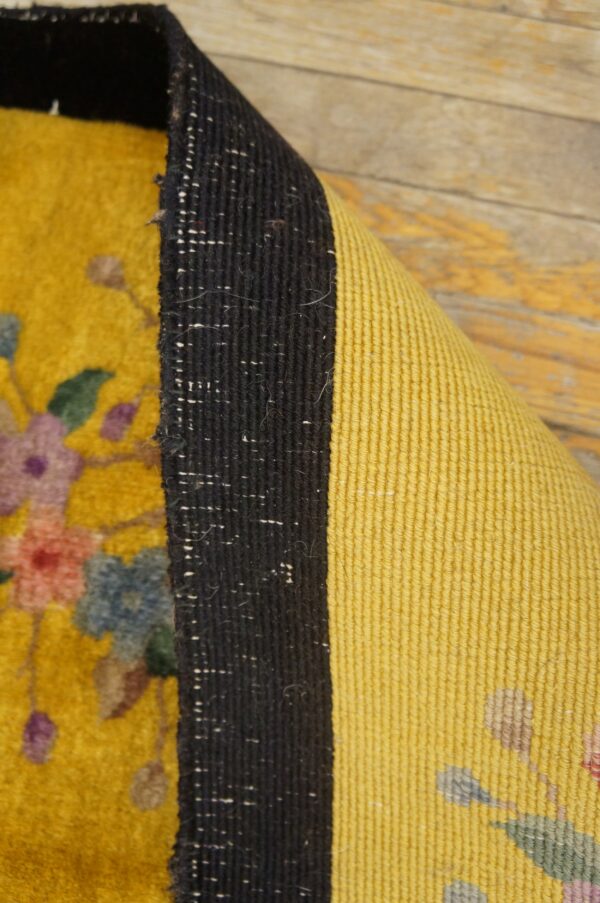 High-pile yellow floral rug edge curled to show dark binding and ribbed yellow backing on wood.