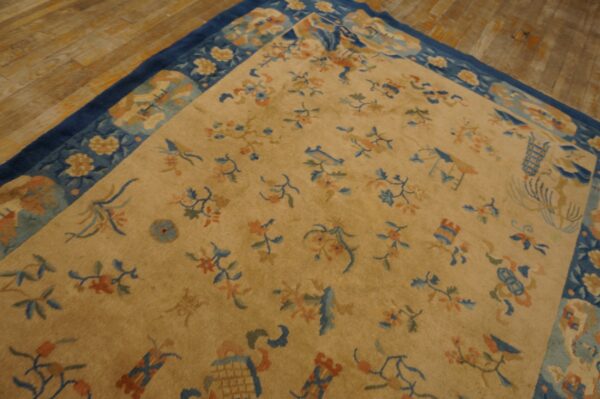 Gold rug featuring scattered blue and coral motifs and a dark blue border, placed on rustic wood flooring.