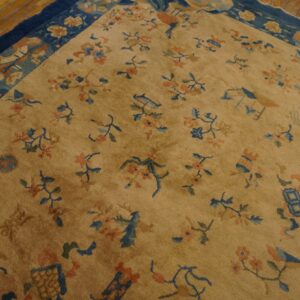 Gold field rug with scattered blue and coral floral motifs and a wide navy border on wood planks.