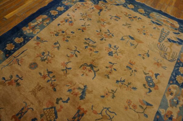 Gold field rug with scattered blue and coral floral motifs and a wide navy border on wood planks.