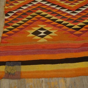 Orange, yellow, and brown flatweave rug with geometric triangle patterns above horizontal color block stripes.