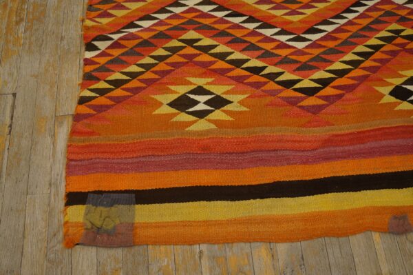 Orange, yellow, and brown flatweave rug with geometric triangle patterns above horizontal color block stripes.