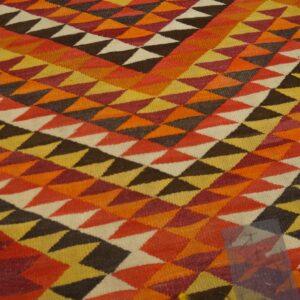 Geometric flatweave rug covered in orange, yellow, rust, and brown triangles resting on light wood flooring.