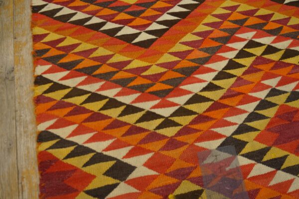 Geometric flatweave rug covered in orange, yellow, rust, and brown triangles resting on light wood flooring.