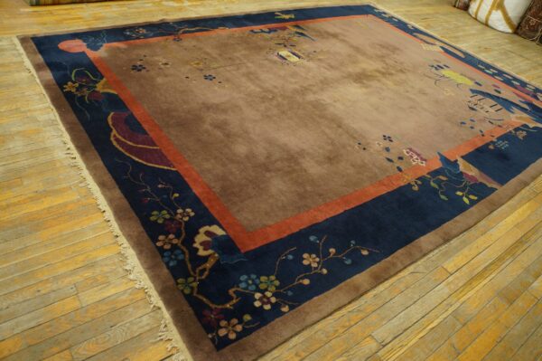 Taupe rug with blue and orange borders featuring floral patterns rests on distressed wooden floorboards.