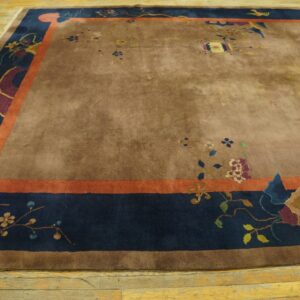 High-pile brown rug with scattered floral designs and a wide navy and orange patterned border on wood floor.