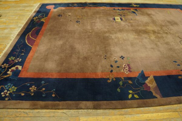 High-pile brown rug with scattered floral designs and a wide navy and orange patterned border on wood floor.