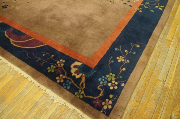 Brown rug with burnt orange and floral navy blue borders resting on distressed yellow hardwood floor planks.